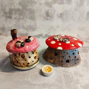 May include: Two ceramic mushroom candle holders with red and white polka dot tops. One holder has a pink top with black ladybirds. A small white tea light candle is in front of the holders.