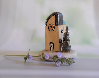 Cerámica hecha a mano decoración casera de una casa de arcilla y un árbol en una piedra de playa natural, regalo de bienvenida