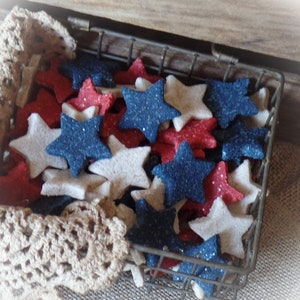 以下が含まれることがあります： 赤い、白、青の星形のオーナメントでいっぱいのワイヤーバスケット。星はキラキラと光っています。