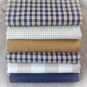 Peut inclure: Pile de huit carrés de tissu dans différents motifs à carreaux. Les tissus sont dans des tons de bleu, marron et beige.