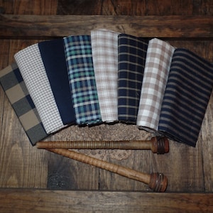 May include: A collection of eight fabric swatches in various shades of blue, brown, and white. The fabrics feature different patterns, including plaid, gingham, and stripes. The swatches are arranged in a fan shape and are displayed on a wooden surface.