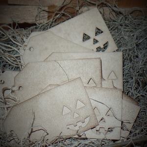 Puede incluir: Un montón de etiquetas de regalo de papel marrón con un diseño de calabaza tallada. Las etiquetas están en una cesta llena de papel triturado marrón.