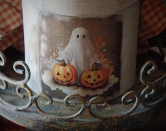May include: A white round box with a vintage Halloween design featuring a ghost and two jack-o'-lanterns. The box is sitting on a decorative metal stand.