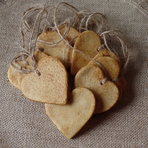 May include: A group of heart-shaped cookies tied together with twine. The cookies are a light brown color and have a speckled texture.