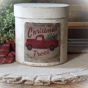 May include: White painted cylindrical container with a vintage Christmas tree delivery label featuring a red pickup truck carrying a Christmas tree. The label reads "Southern Pine Christmas Trees Fresh Cut Free Delivery".
