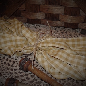 May include: A bundle of yellow and white gingham fabric tied with twine, resting on a crocheted doily. The fabric is frayed at the edges, giving it a rustic look.