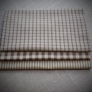 May include: Three brown and beige fabric squares with different patterns. The top square has a brown and beige plaid pattern, the middle square has a brown and beige gingham pattern, and the bottom square has a brown and beige striped pattern.
