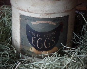 May include: A white, distressed, cylindrical container with a label that reads "All Natural Farm Fresh Eggs". The container is sitting in a bed of green straw.