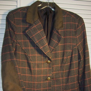 May include: A brown and black plaid blazer with a brown suede elbow patch and three gold buttons. The blazer has a collar and two pockets.