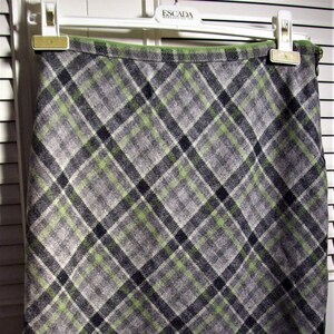May include: A green, gray, and black plaid skirt with a straight hemline. The skirt is made of a soft, woven fabric and has a zipper closure in the back.