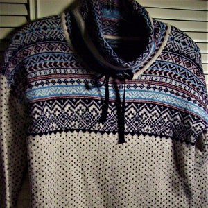 May include: A white sweater with a blue, red, and black patterned design. The sweater has a turtleneck collar with a black ribbon tie.