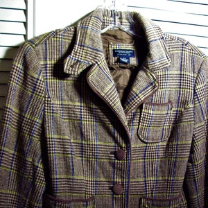 May include: A brown, black, and white plaid blazer with a brown trim and three buttons. The blazer has two pockets and the label "American Rag" is visible on the inside.