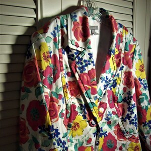 May include: A white blazer with a floral print featuring pink, yellow, and blue flowers. The blazer has a black trim and a single button closure.