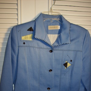 May include: A light blue blazer with black stitching and geometric designs in yellow and black. The blazer has a button closure and a label that reads "Canvasbacks".