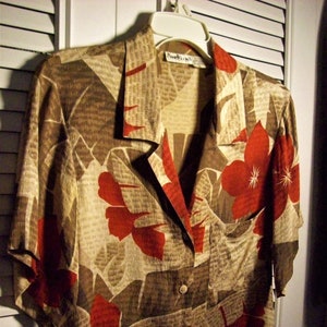 May include: A beige and brown button-up shirt with a red floral pattern. The shirt has a collar and short sleeves. The label on the shirt reads "Ramona Hill".