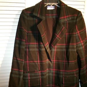 May include: A long black, green, and pink plaid coat with a collar and two pockets. The label on the coat reads "Pendleton".