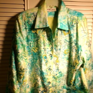 May include: A button-down jacket with a vibrant abstract pattern in shades of green, blue, and yellow. The jacket features intricate beadwork and the label "D'ANAGE" on the collar. The jacket is hanging on a hanger.