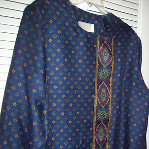 May include: A blue long-sleeved blouse with a patterned design. The blouse has a decorative trim down the front with a variety of colors, including red, green, and gold.