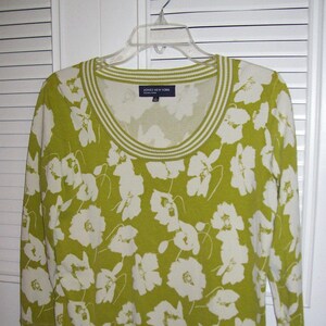 May include: A green sweater with a white floral pattern and a white ribbed neckline. The sweater has the text "Jones New York" on the front.