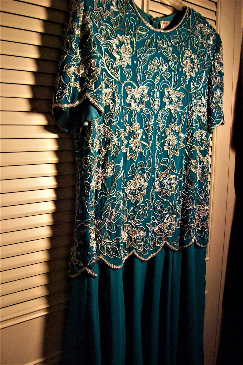 May include: A teal blue dress with a silver and white floral pattern. The dress has a short sleeve and a flowing skirt.