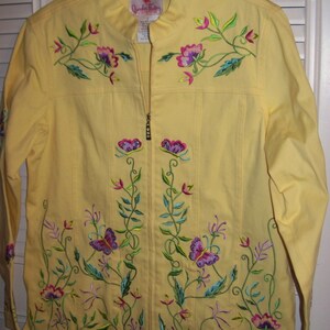 May include: A yellow jacket with a full-length zipper and floral embroidery. The embroidery features purple flowers, green leaves, and butterflies. The jacket is hanging on a clear plastic hanger.