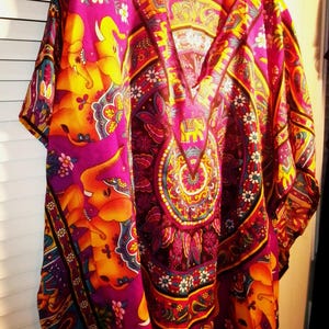 May include: A purple and orange kaftan with an intricate pattern of elephants and paisley designs. The kaftan has a V-neck and short sleeves.