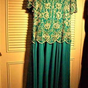 May include: A teal blue formal dress with a beaded, floral pattern in gold and silver. The dress has a fitted bodice and a flowing skirt.