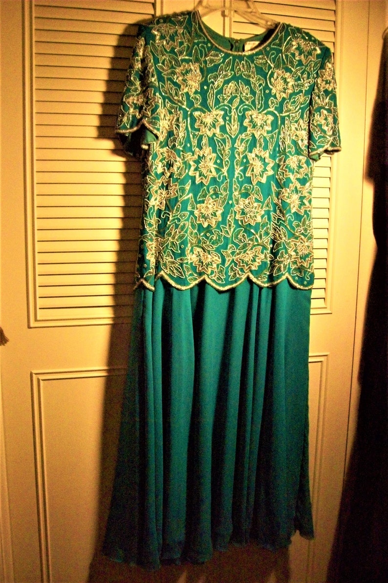May include: A teal blue formal dress with a beaded, floral pattern in gold and silver. The dress has a fitted bodice and a flowing skirt.