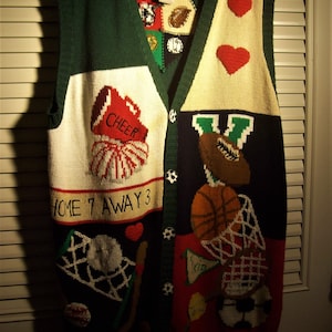 May include: A green, white, red, blue, and black knitted vest with a variety of sports-themed designs, including basketballs, footballs, baseballs, and a cheerleader. The vest has a button closure and the text "HOME 7 AWAY 3" and "CHEER" are visible.