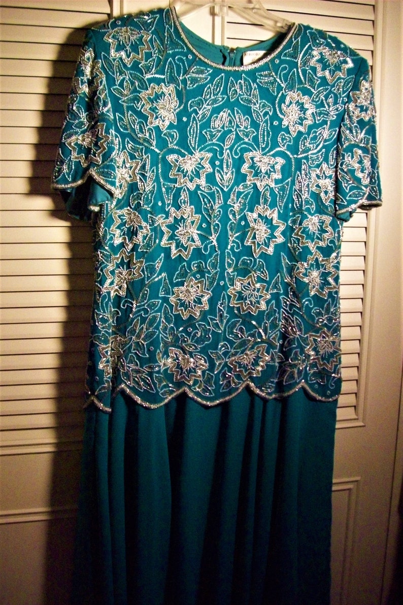 May include: A teal blue dress with a silver and white floral pattern. The dress has a scalloped hemline and a fitted bodice.