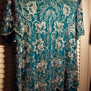 May include: A teal blue dress with a silver floral pattern. The dress has short sleeves and a scalloped hemline.