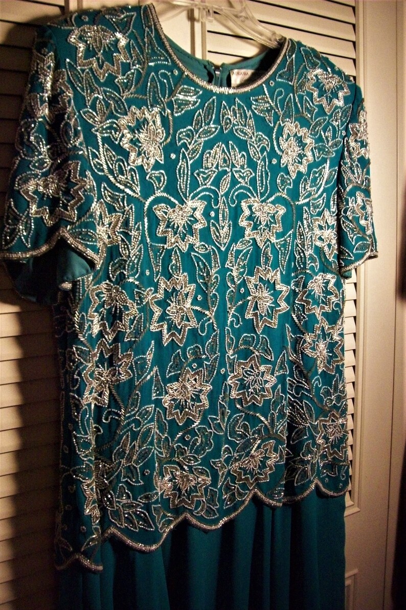 May include: A teal blue dress with a silver floral pattern. The dress has short sleeves and a scalloped hemline.