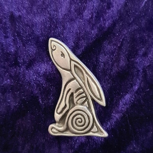 May include: A silver-colored pewter rabbit figurine with a spiral design on its back. The rabbit is sitting upright with its ears perked up.