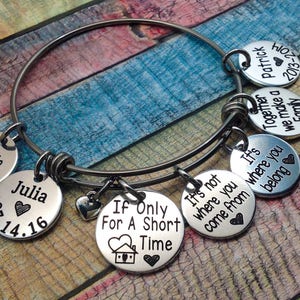 May include: A silver charm bracelet with multiple charms, including a heart, a house, and several round charms with engraved text. The text on the charms includes "Kassie 2015", "Julia 07.14.16", "Together we make a family", "Patrick 2013-20", "It's not where you come from", and "If Only For A Short Time".