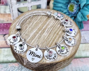 Pode incluir: Um bracelete de prata com pingentes com os nomes Mimi, Abigail, Remington, Hunter, Reed, Roxy, Paxton e Tripp. Cada pingente tem uma pequena gema colorida.