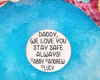 May include: A blue agate coaster with a white round disc on top. The disc has the text "Daddy, we love you stay safe always! Abby Andrew Lucy" printed on it.