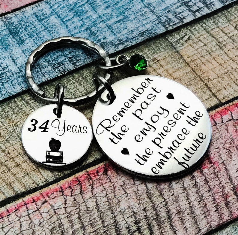 May include: A silver keychain with two charms. One charm is round and says "Remember the past enjoy the present embrace the future". The other charm is round and says "34 Years" with an apple and books graphic.