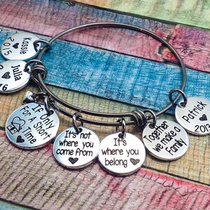 May include: A silver charm bracelet with multiple charms, including a charm that says "If Only For A Short Time", a charm that says "Together We Make A Family", and a charm that says "It's Not Where You Come From, It's Where You Belong".