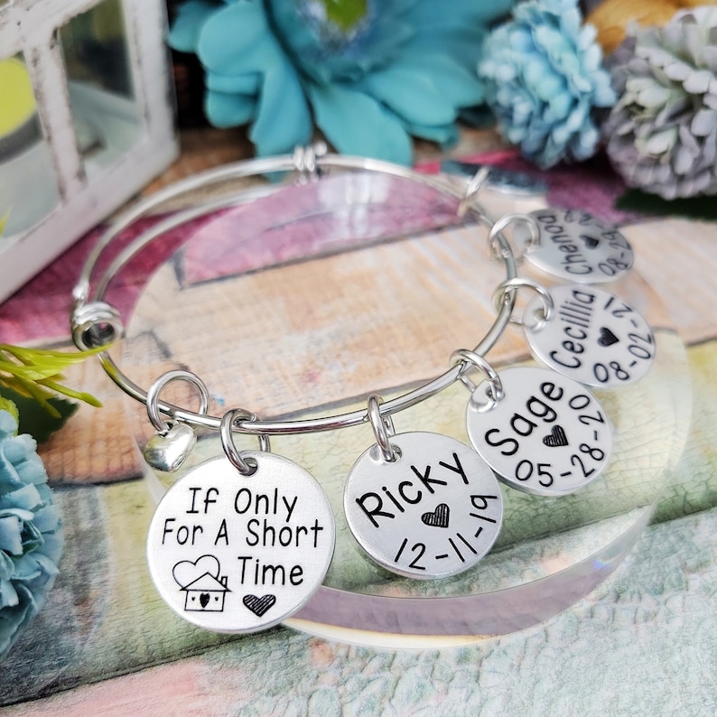 May include: A silver bangle bracelet with five charms. The charms are round and have engraved text, including "If Only For A Short Time", "Ricky 12-11-19", "Sage 05-28-20", "Cecilia 08-02-21", and "Chenoo 08-28-22".