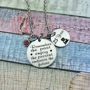 May include: Silver necklace with two round charms. The larger charm has the text "Remember the past enjoy the present embrace the future". The smaller charm has the text "25 Years" and a small image of a book.