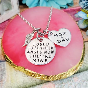 May include: Silver necklace with a heart charm that says "Mom & Dad" and a round charm that says "I used to be their angel now they're mine". The necklace also has a small angel wing charm.