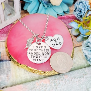 May include: Silver necklace with three charms: a wing, a heart that says "Mom & Dad", and a round charm that says "I used to be their angel now they're mine".