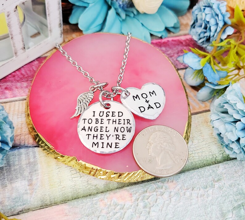 May include: Silver necklace with three charms: a wing, a heart that says "Mom & Dad", and a round charm that says "I used to be their angel now they're mine".