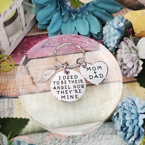 May include: Silver keychain with a heart charm that says "Mom & Dad" and a round charm with an angel wing and the text "I used to be their angel now they're mine".