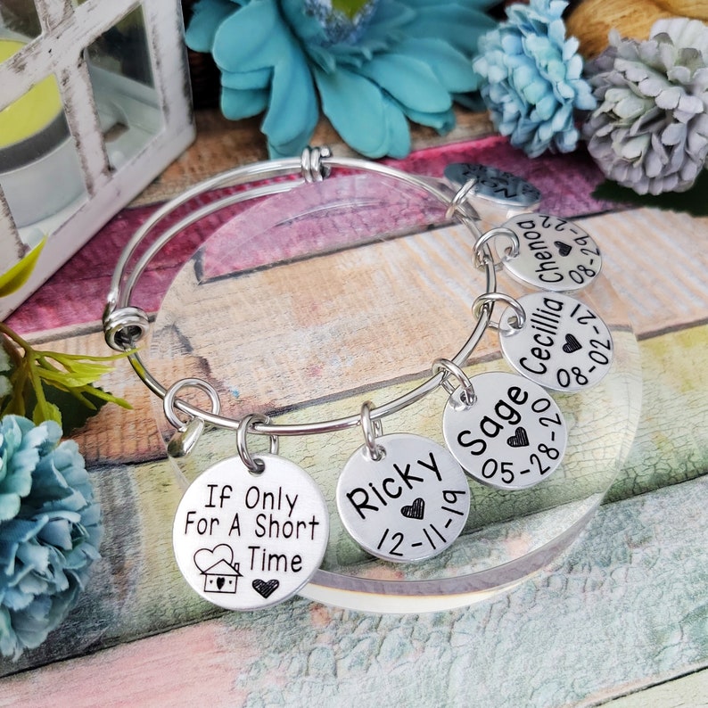 May include: Silver charm bracelet with six charms. The charms are round and have names and dates engraved on them. The charms read "Ricky 12-11-19", "Sage 05-28-20", "Cecillia 08-02-21", "Chenog 08-29-22", and "If Only For A Short Time".