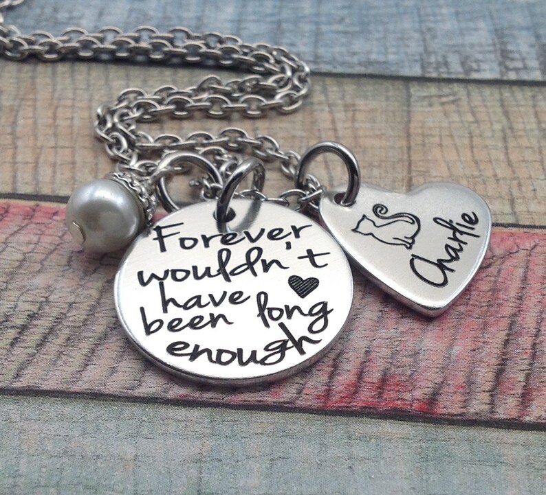 May include: Silver necklace with a round charm that reads "Forever wouldn't have been long enough" and a heart-shaped charm with a cat silhouette and the name "Charlie" engraved on it.