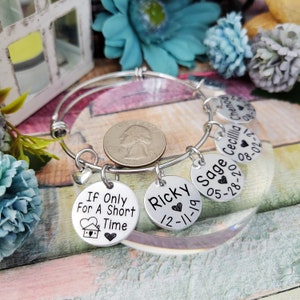 May include: A silver charm bracelet with multiple charms. The charms are round and have engraved text, including names and dates. The charms are attached to a silver bangle bracelet.
