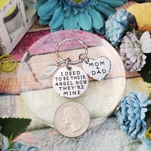May include: Silver keychain with a round charm that reads "I used to be their angel now they're mine" and a heart charm that reads "Mom & Dad".