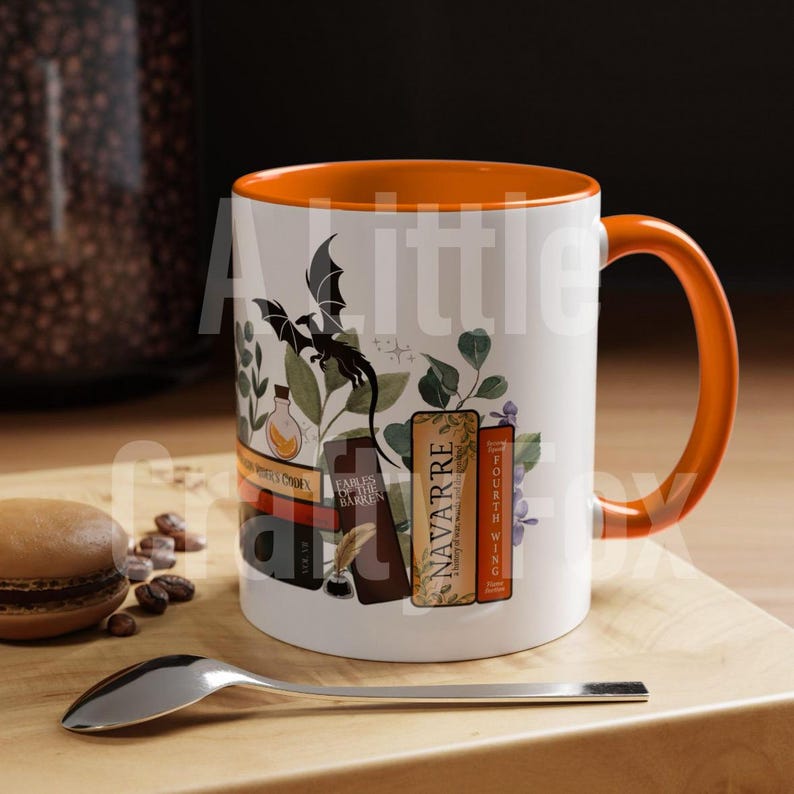 May include: A white ceramic mug with an orange rim and handle. The mug features a black dragon, a vial, a quill pen, and inkwell, and five books with titles including "Navarre" and "Fourth Wing".