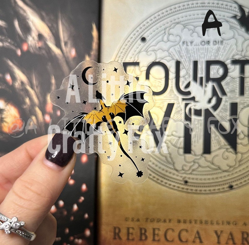 May include: A clear sticker with a gold and black dragon flying through a field of stars. The sticker says "A Little Fourt" and has a crescent moon in the upper left corner.